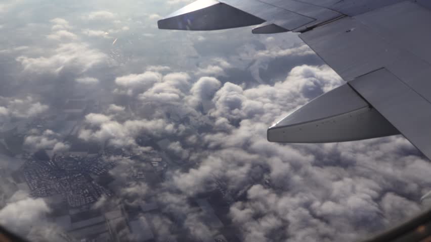Breathtaking aerial view from an airplane window, flying over a stunning landscape of clouds and land. An aircraft wing is in the foreground