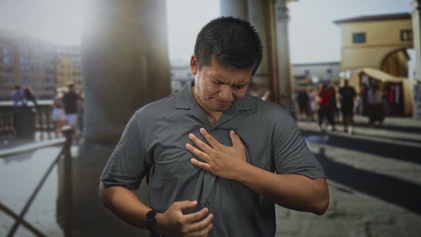 Man clutching chest on a crowded historic street, hand on chest, grimacing as if heartattack; urgent pain.