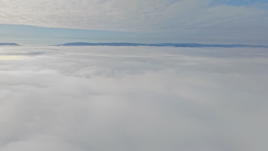 A panoramic aerial view rising above a sea of clouds with mountain peaks in the background