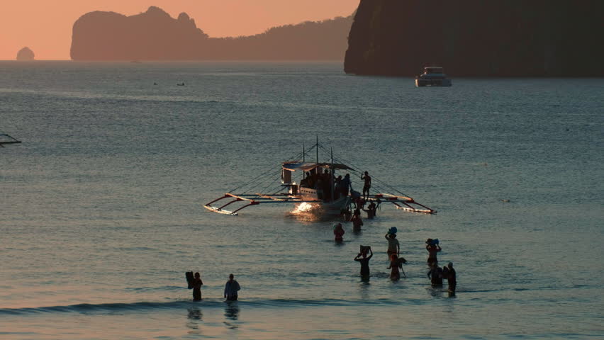 Tourists wading near a traditional outrigger boat on a tropical beach
