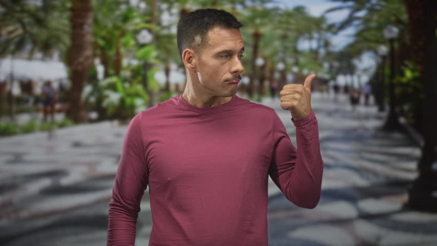 Man forms heart with hands on a palm lined street, wearing maroon long sleeve shirt and wristwatch; affection charm.