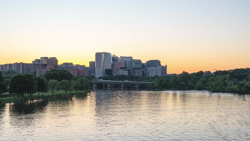 Arlington, Virginia, scenic static 4K timelapse video capturing the transitioning gradient sky over the illuminated Rosslyn skyline as office lights flicker and ripples move across the Potomac River at sunset.