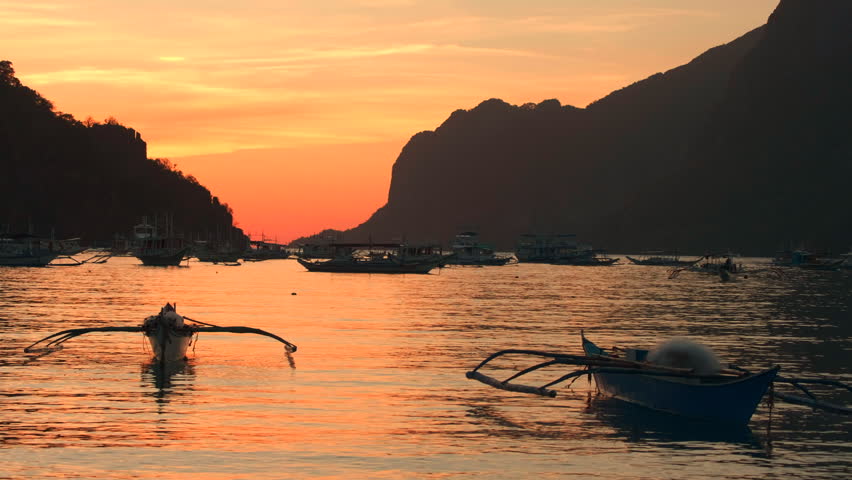 Traditional Filipino bangka boats floating in calm waters during sunset in El Nido