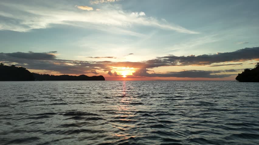 Golden tropical sunset over calm ocean with dramatic clouds and island silhouettes