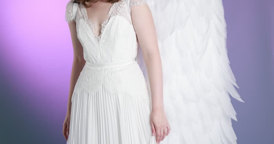 Beautiful girl dressed as angel on violet gradient background, camera moving up