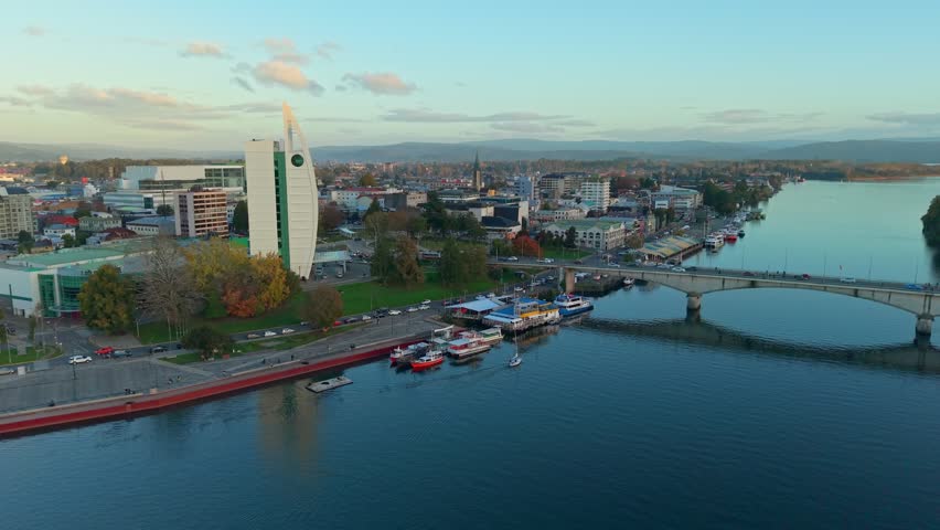 Panoramic aerial orbit ascending over the city of Valdivia, Chile, at dawn, with the bridge and the Dreams Pedro de Valdivia Hotel