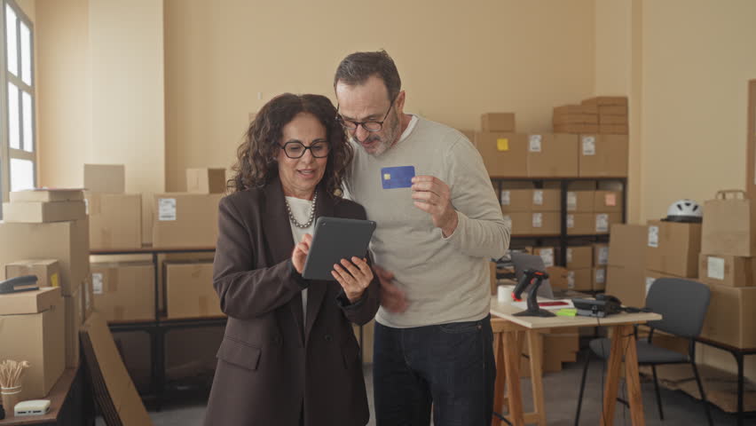Man and woman pointing at tablet while man holds creditcard inside a storage building; efficient collaboration trust.