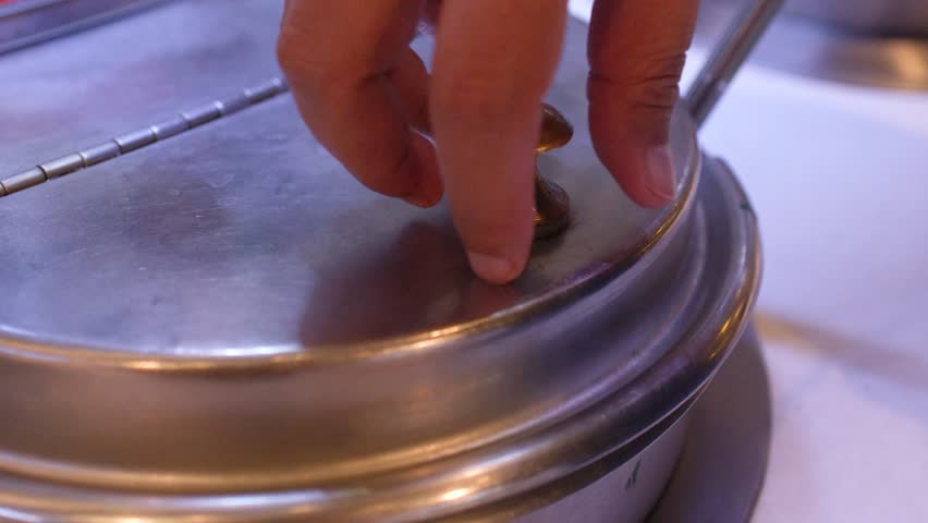 Close-up shot of a hand opening a stainless steel lid and ladling soup into bowls.