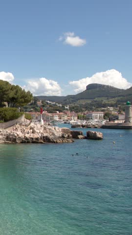 Static wide shot of a rocky coastline and harbor under a bright sunny sky.