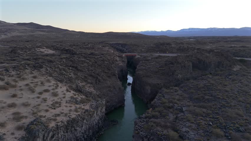 Stunning aerial footage flying over a deep river canyon carved through ancient volcanic rock in La Payunia Reserve, Mendoza, Argentina. Sparse desert landscape
