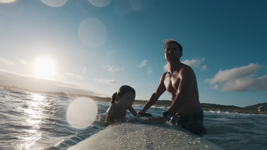 Kid surfs. Little girl learns surfing with her father and tries to keep balance on the surf board