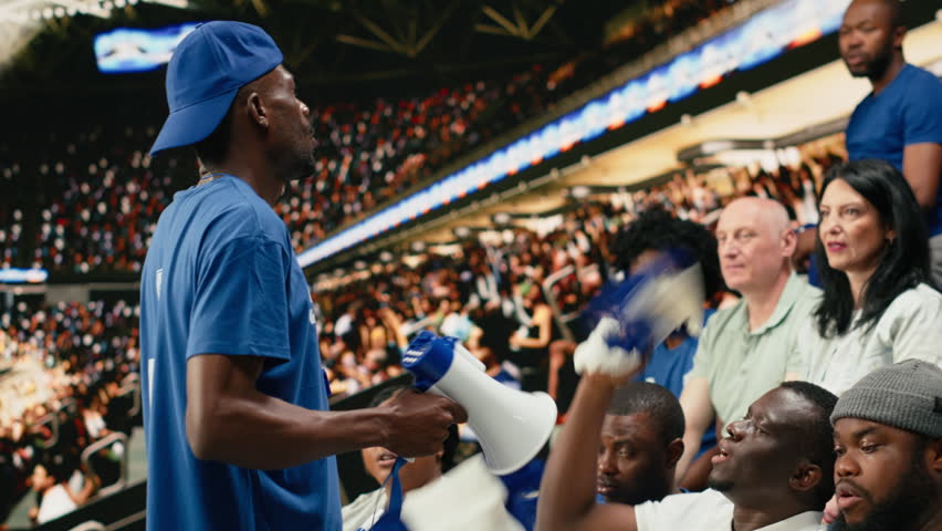Diverse blue football supporters raising arms and chanting together in stadium stands during live soccer match with powerful crowd energy.