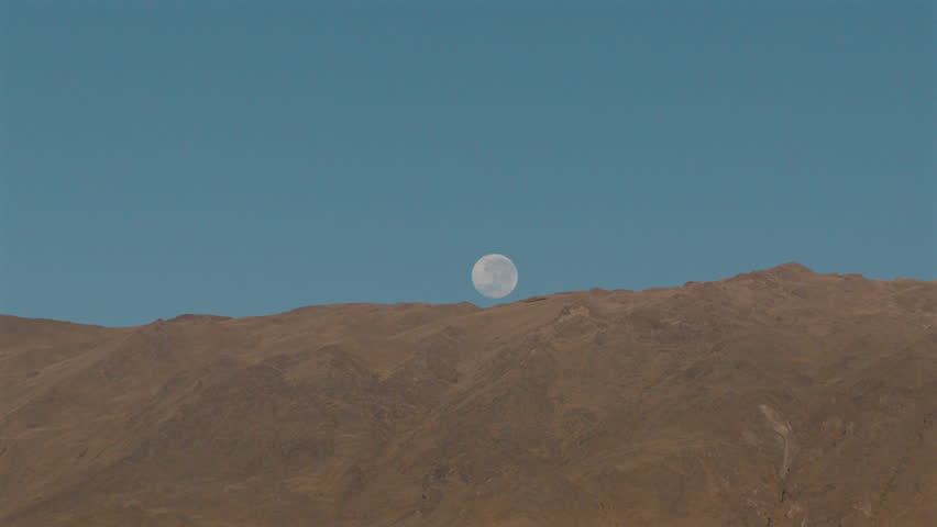 Brilliant full moon rising over the deep brown crests of the Calchaquíes mountain range at dusk. Right tracking aerial.