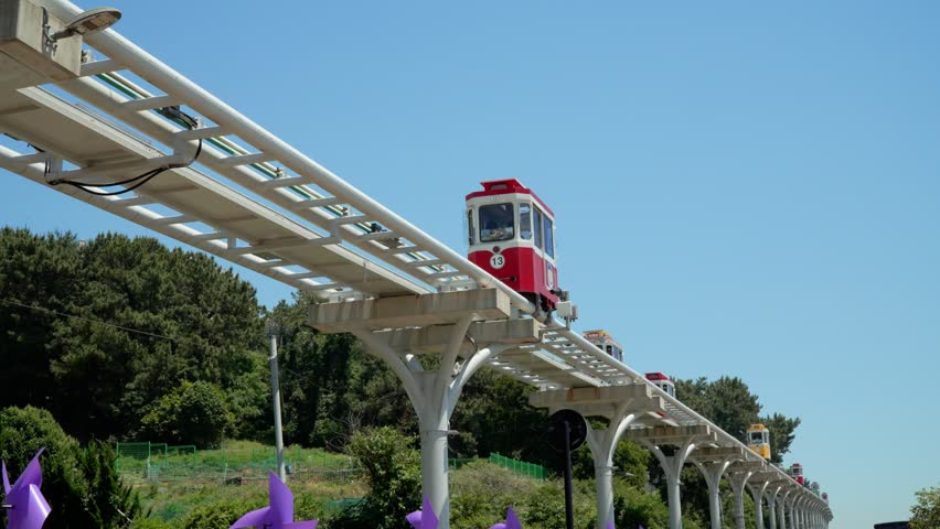 Low angle of colorful retro Sky Capsule cars carrying tourists on elevated track in Haeundae Blue Line Park against blue sky on summer day in Busan Korea