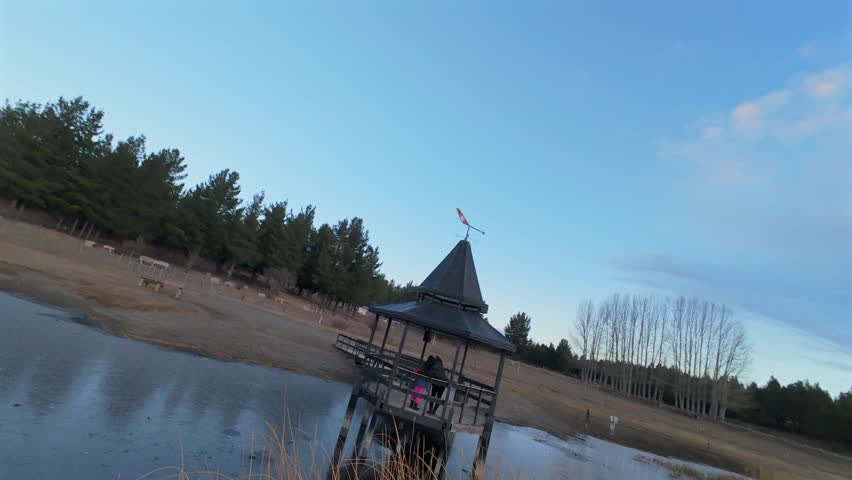 Laguna La Zeta near Esquel, Chubut, Argentina, featuring lakeside pavilion, wooden docks, reed wetlands and Patagonian forest landscape under evening sky, FPV orbit and forward flight shot.