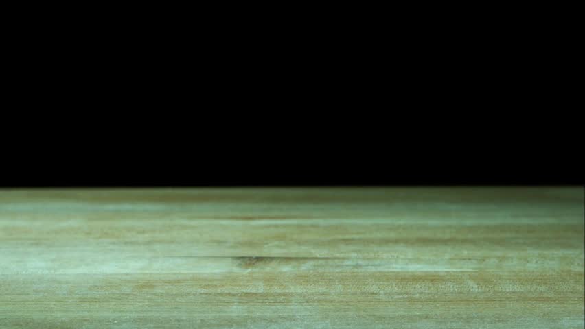 Fresh purple garlic cloves falling and bouncing on a rustic wooden table surface against a solid black background in slow motion for cooking concept