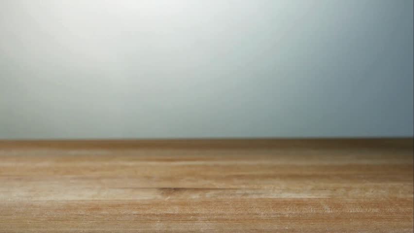 Purple garlic cloves falling and bouncing on a rustic wooden table surface in slow motion against a neutral background showing the texture of the organic vegetable
