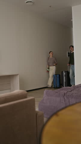 Vertical video of Caucasian young adults entering hotel room with suitcases while young child runs to bed. Ideal for family vacation promos and travel booking advertisements