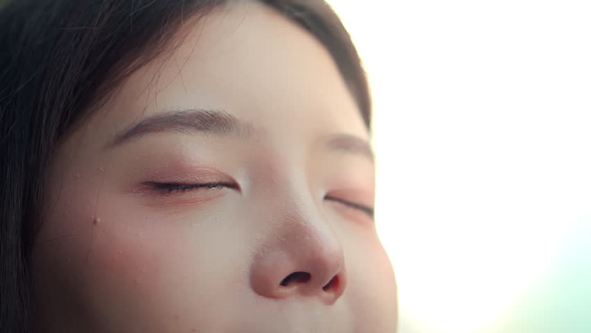 Close up macro shot of young Asian woman slowly opening her brown eyes and looking forward with hope. Beautiful female face showing clean skin, natural eyelashes, and peaceful expression for skincare, mental health, and wellness concept.