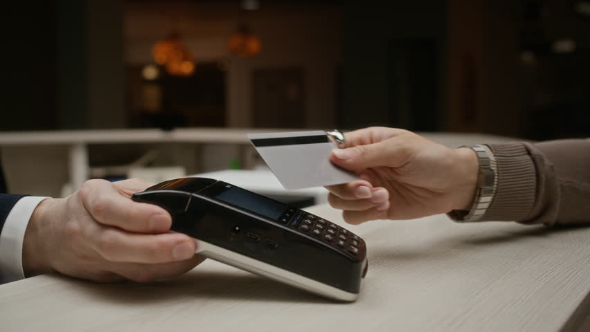 Cropped shot of female guest paying with credit card at hotel reception desk, tapping card on terminal and entering PIN code. Clip is ideal for banking, and contactless payment commercials