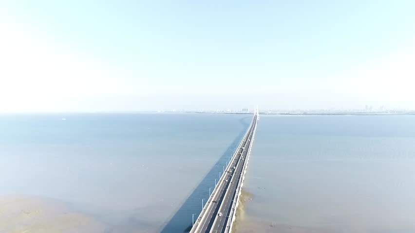 Aerial view of Suramadu long bridge with moving drone backwards revealing green coastal landscape and residential area near the sea.