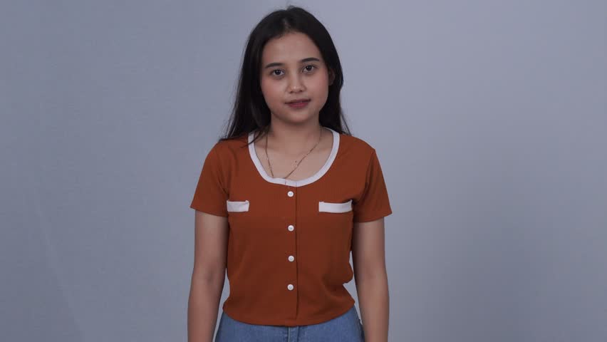A young Asian woman wearing an orange t-shirt and jeans is wearing a black headset enjoying music as seen from the front.