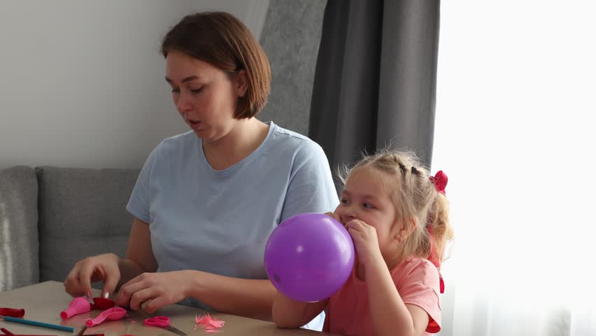 Caucasian woman and young girl enjoying arts and crafts while preparing colorful balloon decorations. Learning through play and child development concept.