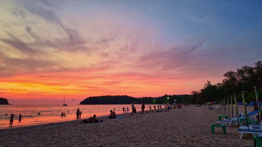 Vibrant seascape featuring dramatic sunset colors reflecting across the water with soft waves rolling onto the sandy shore.