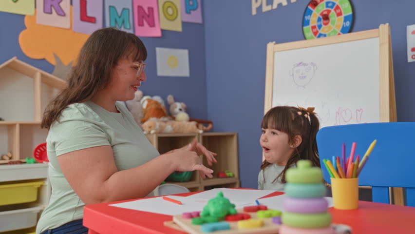 Woman high fives girl with raised hands over crayons and paper in school building; learning bond joy.
