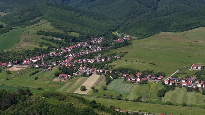 An aerial perspective of a charming village nestled within a lush green valley in rural Hungary during the summer season.