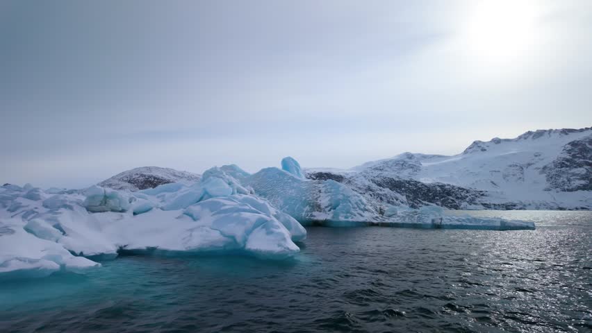 Floating iceberg in calm Arctic waters by snowy Greenland mountains