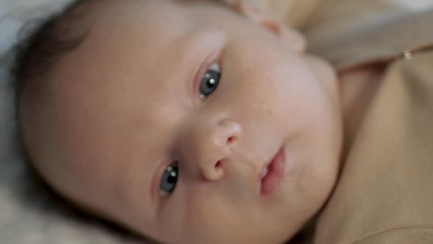 Close-up portrait of a cute newborn baby with beautiful blue eyes looking at the camera
