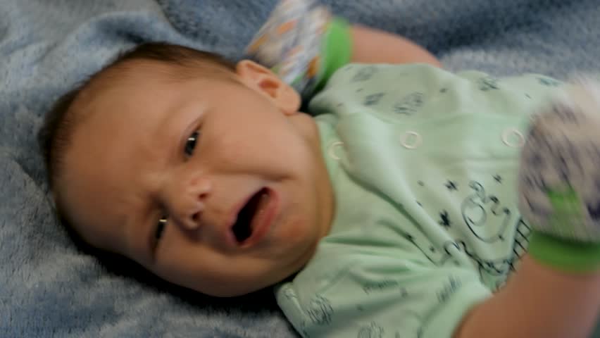 Cute newborn baby boy with blue eyes lying on his back on a soft blue blanket making funny faces