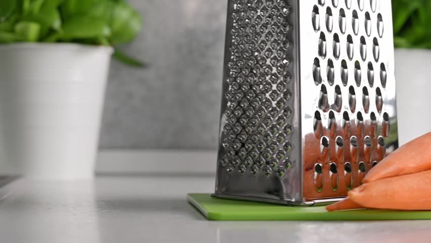 Fresh carrots and metal grater on kitchen countertop create clear food preparation scene. Carrot ingredient concept highlights natural produce, wholesome vegetable nutrition and healthy cooking workflow