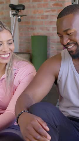 Vertical video: Panning camera, woman in pink top responding to partner, smiling at home gym, bike. Couple, fitness, studio, brick, minimalist, casual, vertical video