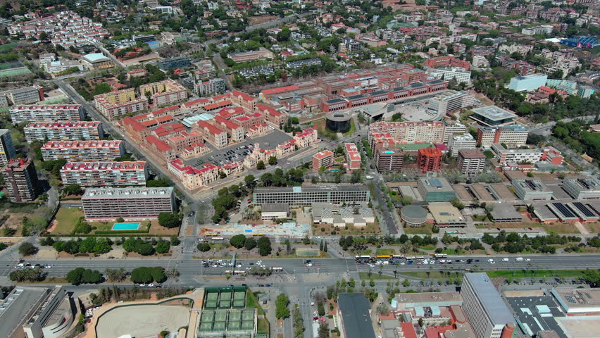 High angle drone footage showing the Avinguda Diagonal road and the University of Barcelona campus buildings with traffic and residential blocks in Barcelona, Spain on a sunny day.