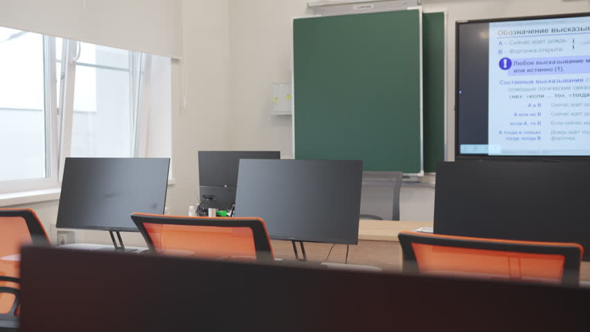 Large interactive screen displays presentation next to green chalkboard. Contemporary school study workspace looks clean and tidy