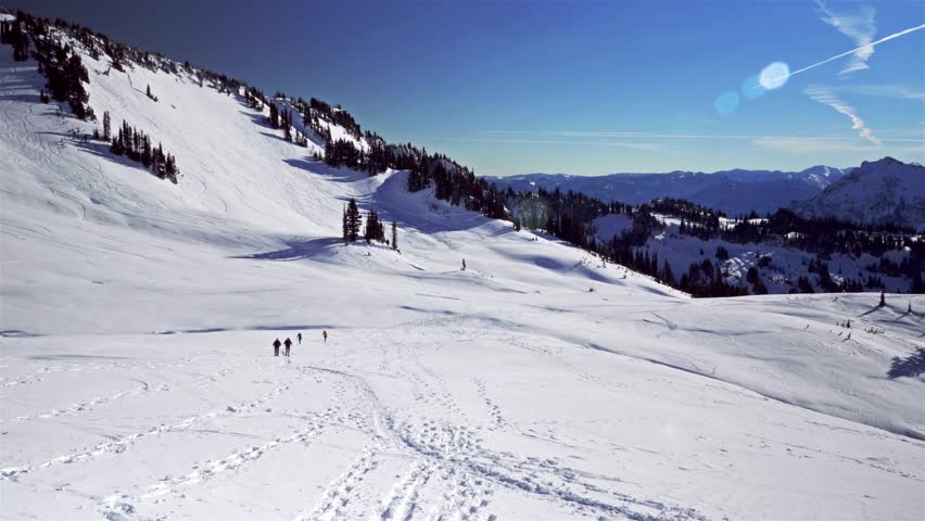 Footage of hikers snowshoeing along the snowy Skyline Trail in the Paradise area of Mount Rainier National Park, Washington State, on a clear, sunny winter day. The trail offers expansive panoramic vi