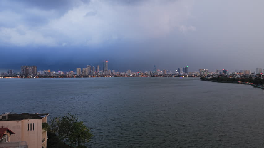 Dramatic wide shot of a lightning storm approaching the Hanoi skyline across West Lake. Cinematic weather event suitable for news, climate change, or travel documentaries.