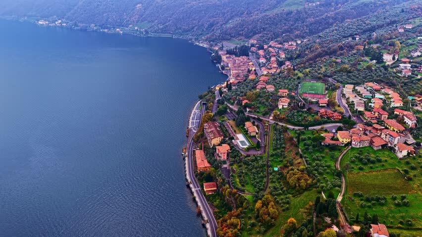 Aerial Drone Pushing Forward Over Scenic Lakeside Village With Olive Groves and Red Rooftops Along the Shores of Lake Iseo Portraying the Hidden Gem of Italian Lakes