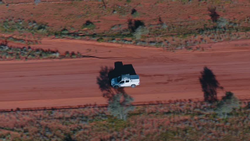 Majestic aerial view of a white 4x4 vehicle driving along a remote dusty road through the vast, arid landscape of the Namibian desert, a perfect representation of an African safari adventure