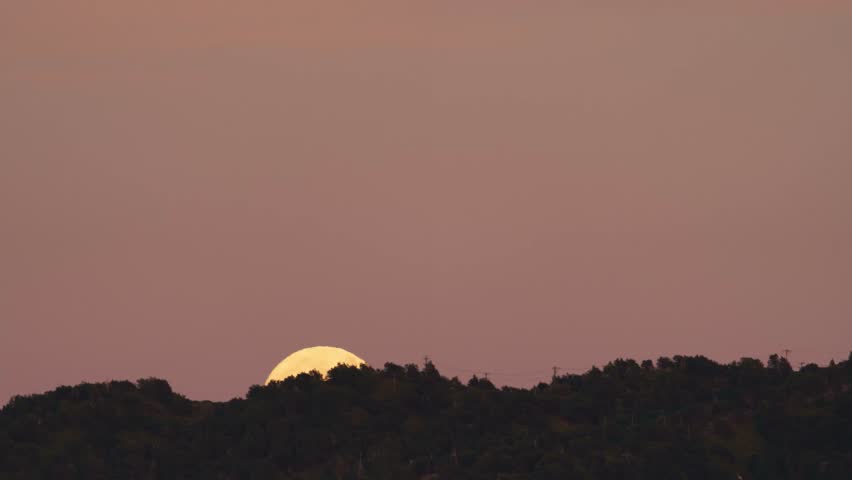 Timelapse of the full moon rising over a mountain ridge at sunset, filmed from Lake Arrowhead, looking toward the San Bernardino National Forest, California.