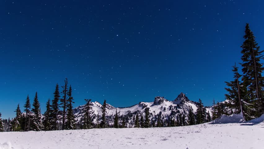 A long-exposure shot of the night sky filled with stars above the snow-covered peaks and evergreen trees along the Skyline Trail and Panorama Point area in Mount Rainier National Park, Washington Stat