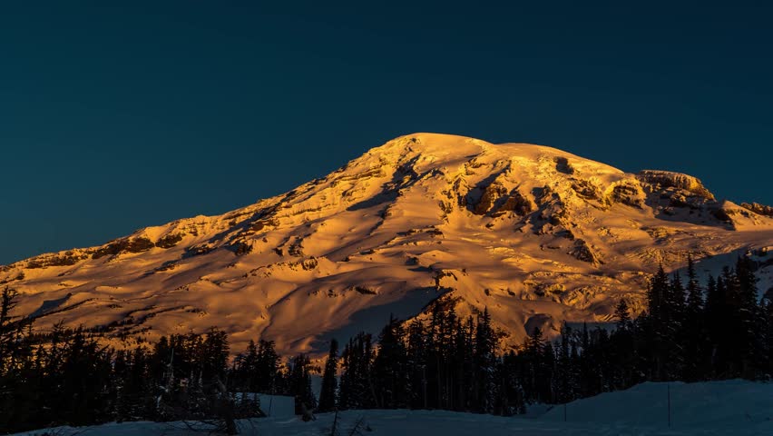 Scenic winter footage of the iconic Mount Rainier in Mount Rainier National Park, Washington, USA, during the beautiful light of sunset or sunrise. The snow-covered landscape, a winding road, and ever