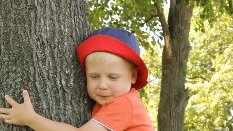 Blonde young happy boy on a walk. Nature Park. hug a tree. 