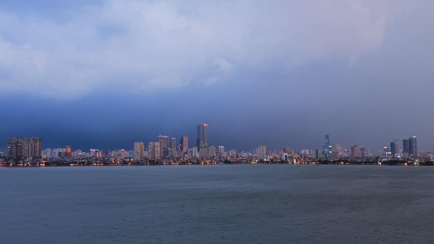 Dramatic cinematic wide shot of a lightning storm flashing over the Hanoi skyline and Tay Ho West Lake during blue hour. Great for weather news and travel documentaries.
