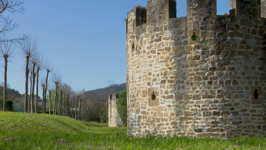 Stone turret and walls of a castle with trimmed trees and grassy field a round
