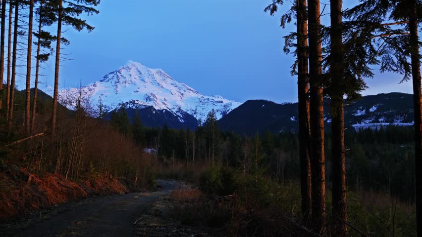 Footage capturing the majestic, snow-capped Mount Rainier volcano as viewed from the forested Mowich Lake Road in Mount Rainier National Park, Washington State, USA.