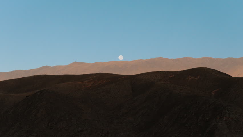 Full moon setting behind mountain ridges during sunrise over Tafí del Valle in Tucumán, Argentina.