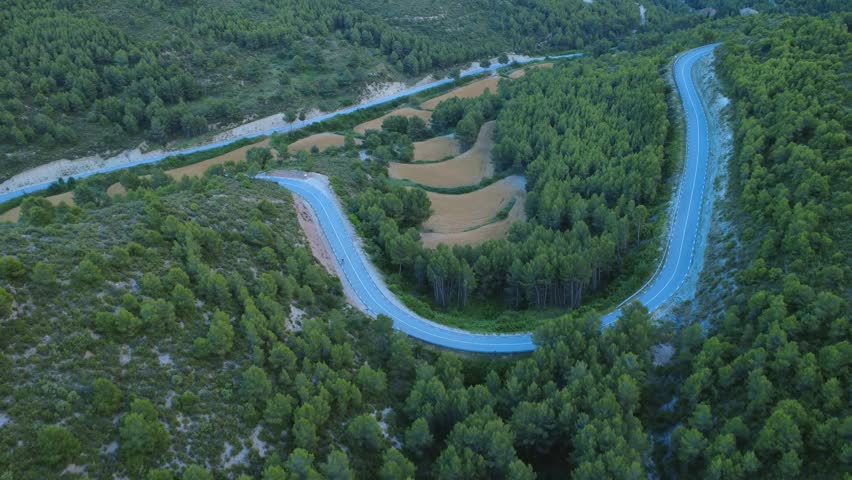 Aerial drone view of a hairpin mountain road through a Mediterranean forest landscape in Catalonia, Spain. Useful for transportation, road trip, scenic route, rural infrastructure, travel, mountain driving, nature and countryside concepts.